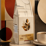 A 12 oz package of Bauhaus Brew coffee stands on a round pedestal, styled with scattered coffee beans and a cup of coffee on a saucer against an abstract geometric background.