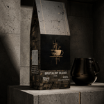 A bag of Brutalist Blend coffee sits on a concrete pedestal in a dark, minimalist industrial setting, with a black ceramic pot beside it.