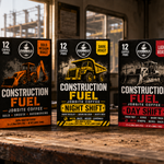 Three Everbold Construction Fuel coffee boxes displayed on a workbench in a construction site setting, alongside a yellow hard hat, rolled plans, and a black Everbold mug.