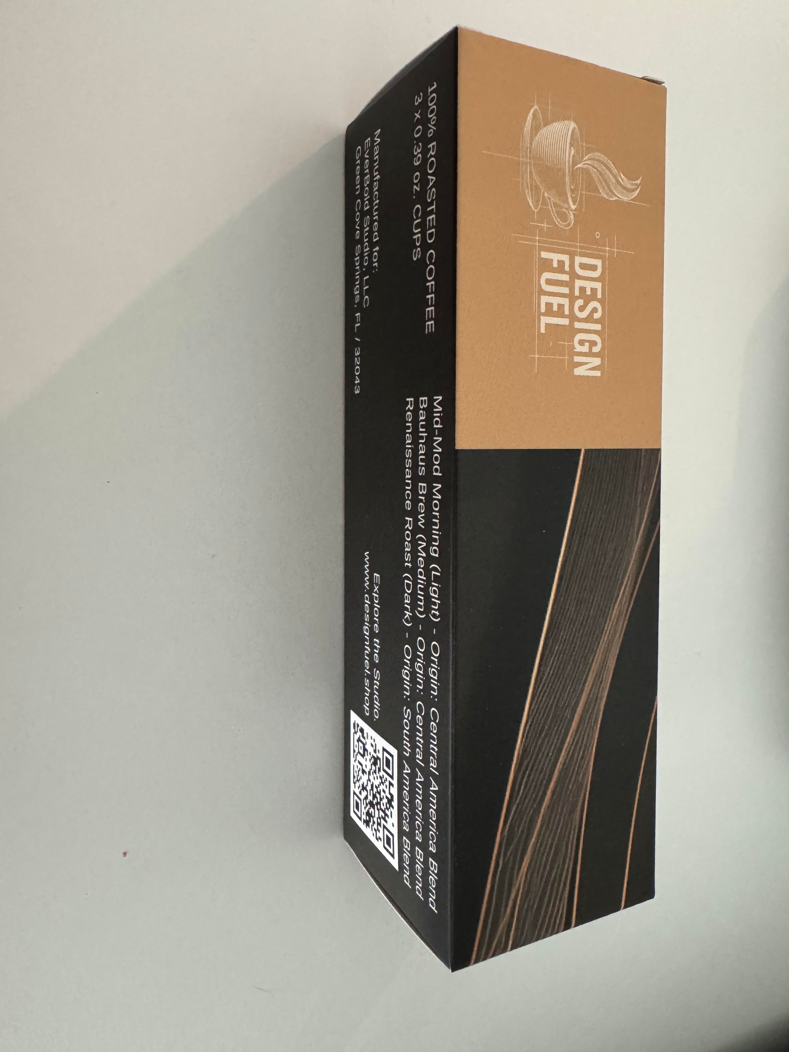 A tall rectangular product box standing upright against a plain light background. The box design is split horizontally: the top half is warm tan/caramel with white 'DESIGN FUEL' text and a small line-art logo, and the bottom half is black with thin warm brown diagonal lines.