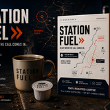 Station Fuel coffee pods packaging and product shown in a dark promotional scene with a coffee mug, a single coffee pod, and a walkie-talkie. The box and mug are white and dark navy with orange accents and the words STATION FUEL.